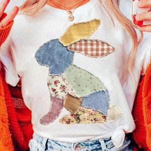 May include: White t-shirt featuring a patchwork bunny design. The bunny is composed of various fabric patterns, including floral, gingham, and solid colors. The shirt is a casual style, suitable for everyday wear.