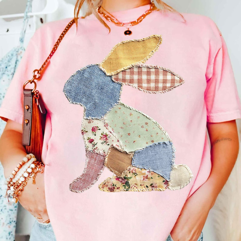 May include: Pink t-shirt featuring a patchwork bunny design. The bunny is composed of various fabric patterns, including floral, gingham, and solid colors. The shirt has short sleeves and a crew neck.