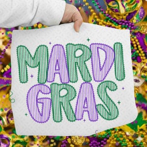 Puede incluir: Un coj&iacute;n cuadrado blanco con las palabras "MARDI GRAS" en letras a rayas verdes y moradas. Las letras tienen un borde festoneado y est&aacute;n decoradas con peque&ntilde;as formas de estrella. El fondo incluye cuentas y m&aacute;scaras de Mardi Gras.