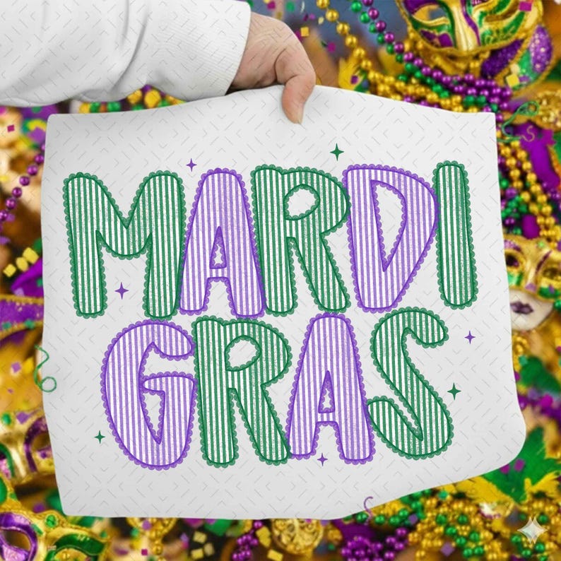 Puede incluir: Un coj&iacute;n cuadrado blanco con las palabras "MARDI GRAS" en letras a rayas verdes y moradas. Las letras tienen un borde festoneado y est&aacute;n decoradas con peque&ntilde;as formas de estrella. El fondo incluye cuentas y m&aacute;scaras de Mardi Gras.