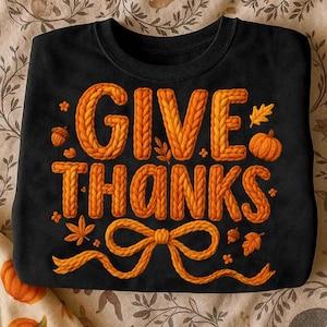 Puede incluir: Sudadera negra con las palabras "GIVE THANKS" en naranja, con letras con efecto de punto. El diseño incluye un lazo, calabazas, hojas y bellotas. Un diseño temático de otoño.