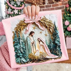May include: A pink square canvas with a religious painting of the Nativity scene. The artwork features Mary, Joseph, and baby Jesus, surrounded by a gold wreath and evergreen trees. A pink bow adorns the top.