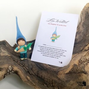 May include: A felt gnome doll with a blue hat and a carrot, next to a card with German text. The card has a gnome illustration and the words "Lern Wichtel". The doll is a charming, handcrafted item.