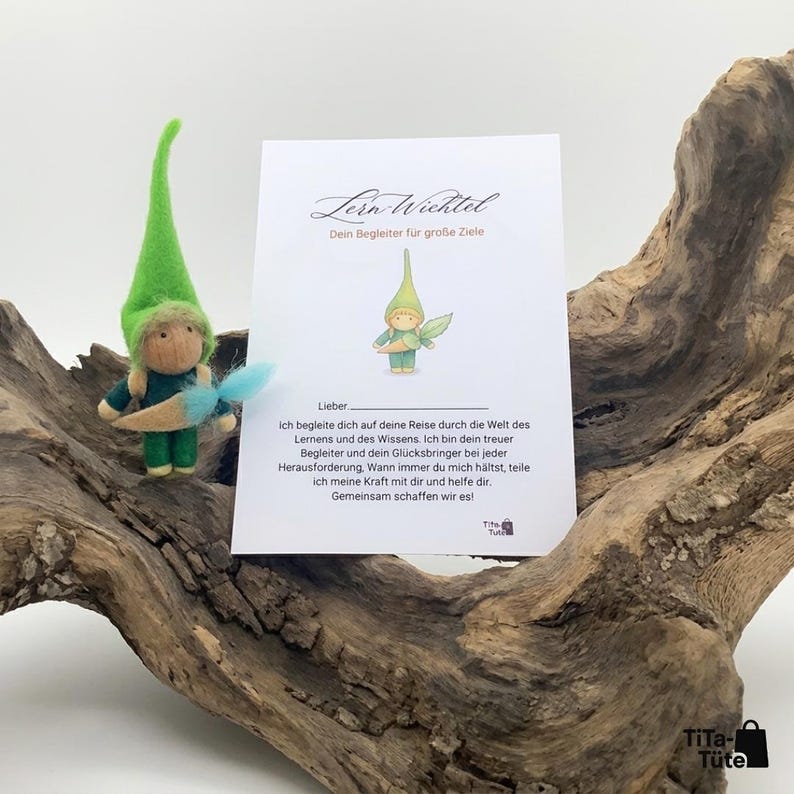 May include: A felt gnome figure with a green hat and blue feather, beside a card with German text. The card shows a drawing of a gnome and the words "Lern-Wichtel Dein Begleiter f&uuml;r gro&szlig;e Ziele."