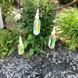 May include: Three hanging ornaments featuring iridescent, multi-faceted glass crystals suspended by thin white strings. Each crystal is topped with a series of small, round, natural light-coloured wooden beads, creating a vertical arrangement.