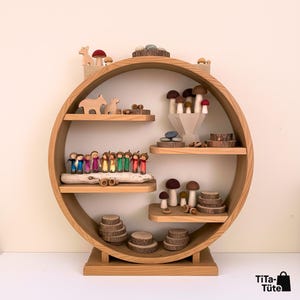 Inspiration für den Waldorf Jahreszeitentisch: Ein rundes Holzregal ist liebevoll dekoriert mit der kompletten, bunten Waldwichtel-Kollektion von TiTa-Tüte. Daneben stehen Holzpilze, Tiere und Holzscheiben. Stimmungsvolle Präsentation von natürlichem Montessori Spielzeug.