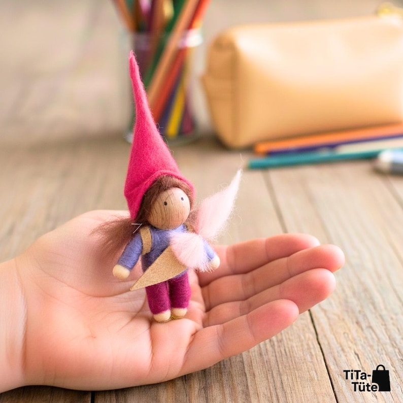 Eine Hand hält einen pinken TiTa-Tüte Schulwichtel fest umschlossen. Der kleine Wichtel dient als Sorgenfresser und Mutmacher für die Hosentasche bei Aufregung