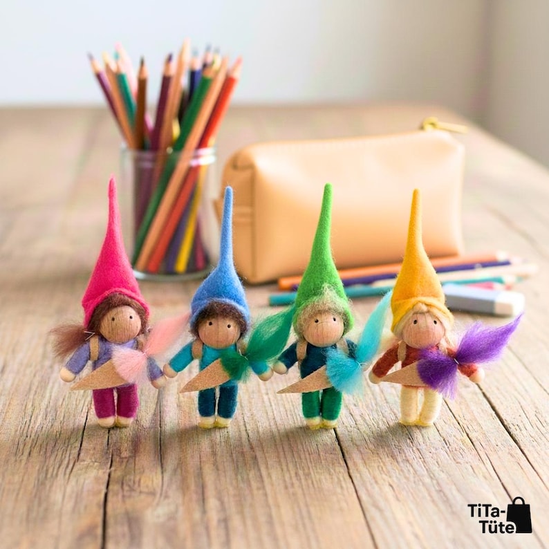 May include: Four handmade felt dolls with wooden heads and colourful pointed hats. Each doll holds a wooden cone and has a fluffy tail. The dolls are arranged on a wooden surface with pencils and a pencil case in the background.