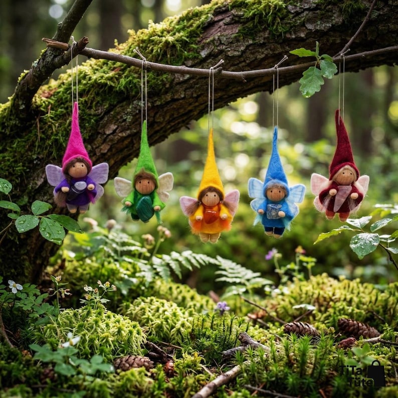 May include: Five whimsical fairy ornaments with pointed hats and delicate wings hang from a tree branch. Each fairy is dressed in a different color: purple, green, yellow, blue, and red. The background is a lush, green forest.