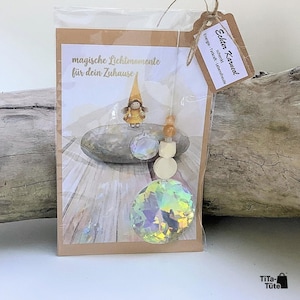 May include: A decorative suncatcher ornament in a clear plastic sleeve with a cardboard backing. The card features a gnome illustration and the text "magische Lichtmomente f&uuml;r dein Zuhause". A tag reads "Echter Karneol". Includes crystal beads.