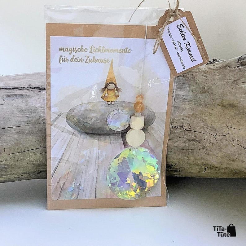 May include: A decorative suncatcher ornament in a clear plastic sleeve with a cardboard backing. The card features a gnome illustration and the text "magische Lichtmomente f&uuml;r dein Zuhause". A tag reads "Echter Karneol". Includes crystal beads.