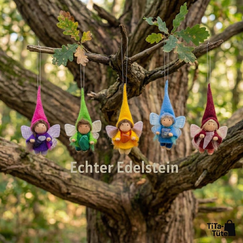 May include: Five colorful felt fairy ornaments hanging from a tree branch. Each fairy has a pointed hat, wings, and a small body. The fairies are in shades of pink, green, yellow, blue, and burgundy. The text "Echter Edelstein" is visible.