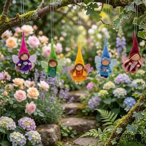 May include: Five hanging fairy ornaments with pointed hats and wings. Each fairy has a different colored hat and outfit, including pink, green, yellow, blue, and burgundy. The fairies are suspended from a tree branch against a blurred garden background.