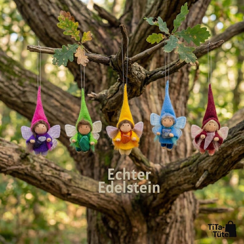 May include: Five whimsical felt fairy ornaments with pointed hats and delicate wings hang from a tree branch. Each fairy is a different color: pink, green, yellow, blue, and burgundy. The text "Echter Edelstein" is visible.