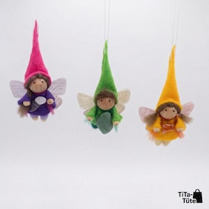 May include: Three handmade fairy ornaments with felt hats and wings. The fairies are dressed in purple, green, and yellow, with wooden faces and brown hair. Each fairy is suspended by a thin string against a white background.