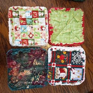 May include: Four handmade Christmas-themed pot holders with a variety of festive patterns, including snowmen, Christmas trees, and Santa Claus. The pot holders are made with a patchwork of different fabrics and have a white crocheted border.