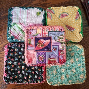 May include: Five handmade quilted pot holders with different patterns. The patterns include a green and white plaid, a yellow and white watermelon print, a pink and purple floral print with the text "Time for Hats", a black and white floral print, and a green and white floral print.