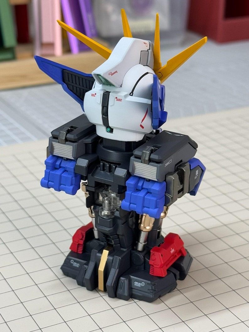 May include: A partially assembled Gundam model kit. The model features a white head with blue and yellow accents, black shoulders, blue arms, and red feet. The model is set against a grid background.