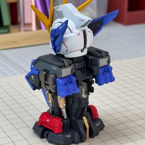 May include: A partially assembled model robot with a white head, blue accents, and yellow spikes. The robot has a black torso with blue and red details. The model is on a grid-lined surface.