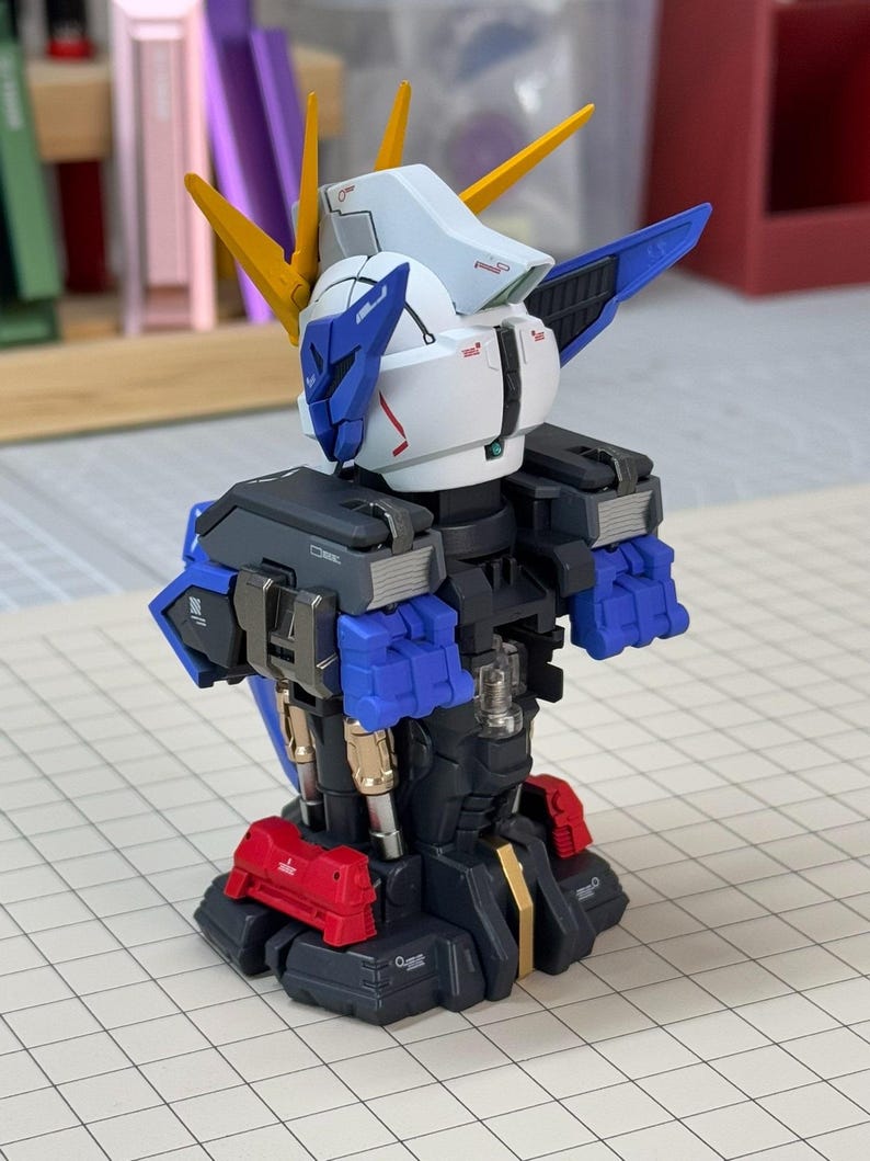 May include: A partially assembled model robot with a white head, blue accents, and yellow spikes. The robot has a black torso with blue and red details. The model is on a grid-lined surface.