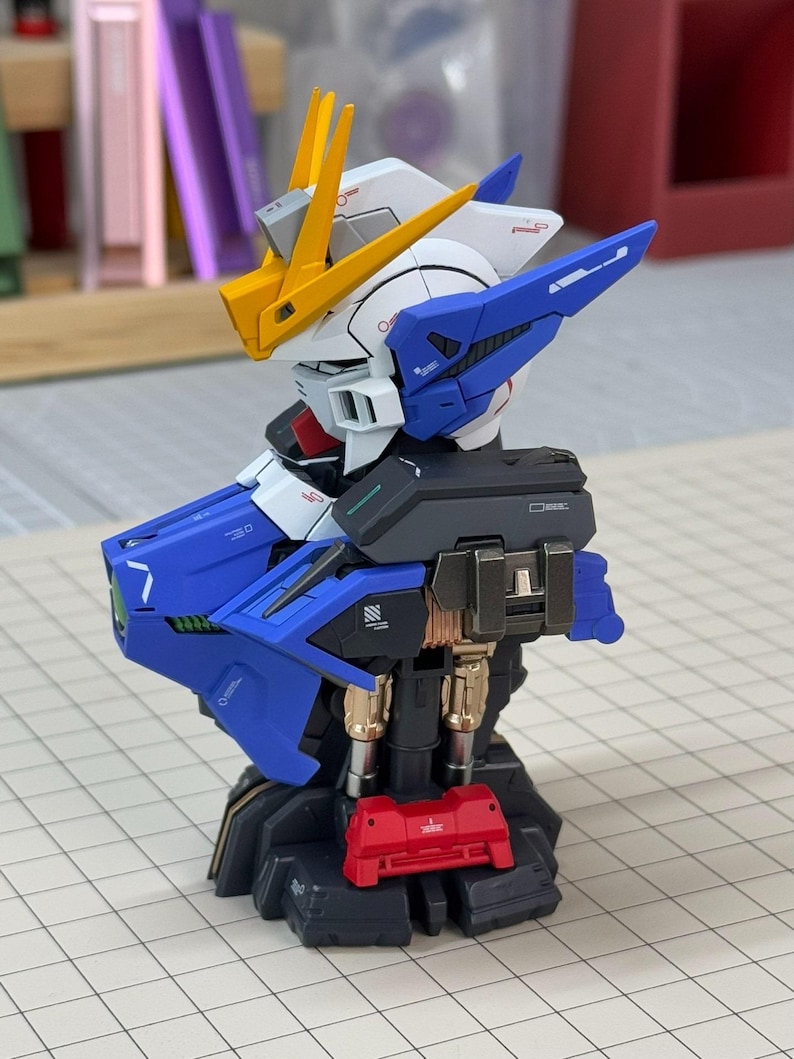 May include: A detailed model of a Gundam robot, featuring a color scheme of blue, white, yellow, and red. The model has intricate mechanical details, including articulated joints and panels. The robot is posed on a grid surface, showcasing its design.