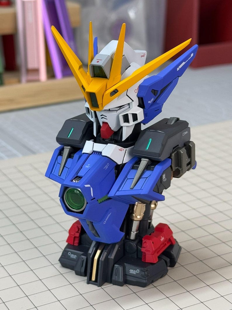May include: A detailed model of a robot with a blue, white, yellow, black, and red color scheme. The robot has a complex design with multiple panels, sharp angles, and a prominent head with yellow antennae. The model is on a grid surface.