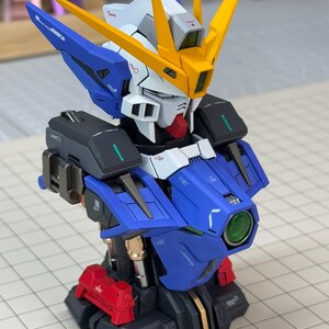 May include: A detailed model of a robot's upper body, featuring a blue, white, yellow, red, and black color scheme. The model has intricate details, including a head with yellow fins, a blue chest, and a red base. The model is a collectible item.