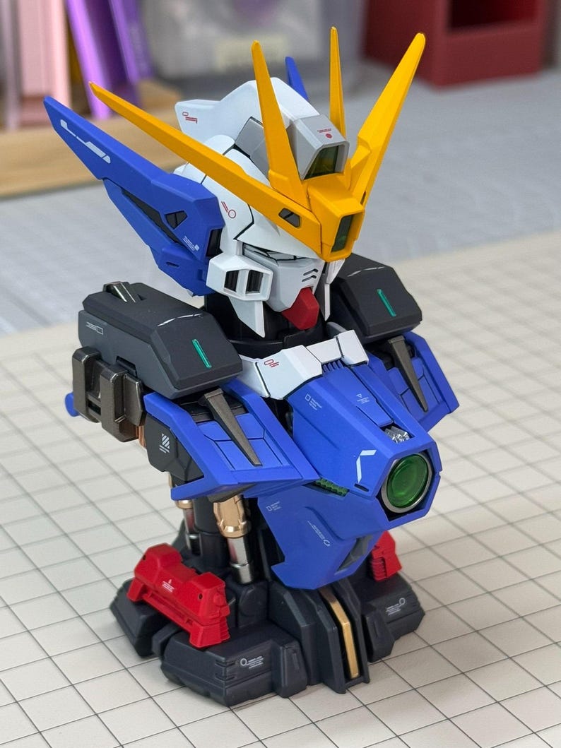 May include: A detailed model of a robot's upper body, featuring a blue, white, yellow, red, and black color scheme. The model has intricate details, including a head with yellow fins, a blue chest, and a red base. The model is a collectible item.