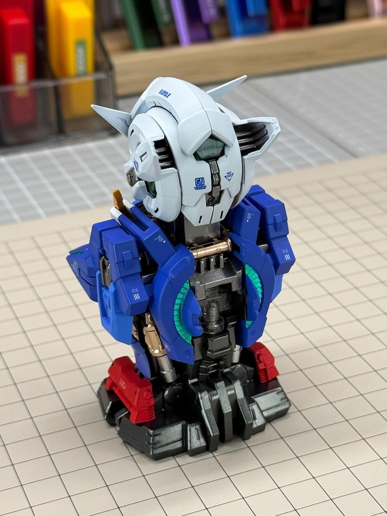 May include: A partially assembled model robot with a white head, blue torso, and red accents. The robot has intricate details and mechanical components, suggesting a hobbyist project or collectible item. The model is set against a grid background.