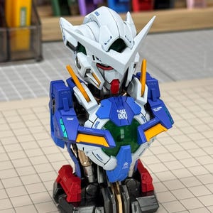 May include: A detailed model of a robot's upper body, featuring a white head with sharp angles, a red face, and blue and yellow accents. The chest area displays the text "000" and is surrounded by blue and gold panels. The base is red and black.