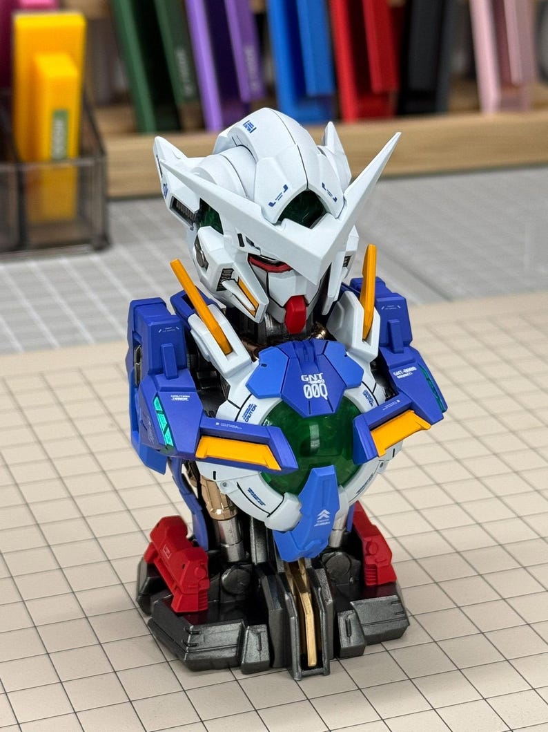May include: A detailed model of a robot's upper body, featuring a white head with sharp angles, a red face, and blue and yellow accents. The chest area displays the text "000" and is surrounded by blue and gold panels. The base is red and black.
