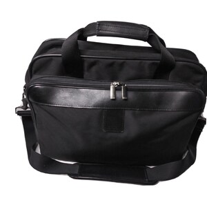 May include: Black briefcase with a top handle and a detachable shoulder strap. The bag has a zippered main compartment and a front pocket with a leather trim. The bag is made of a durable material and is suitable for carrying documents and other essentials.