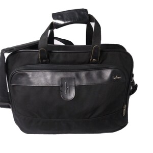 May include: Black briefcase with a leather handle and shoulder strap. The bag has a leather accent across the front with a debossed "h" logo. Features a zippered side pocket and a top handle.