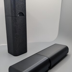 May include: Two black rectangular cases, one upright and the other lying horizontally. The upright case has a textured surface and a curved cutout. The horizontal case is smooth and appears to be hinged.