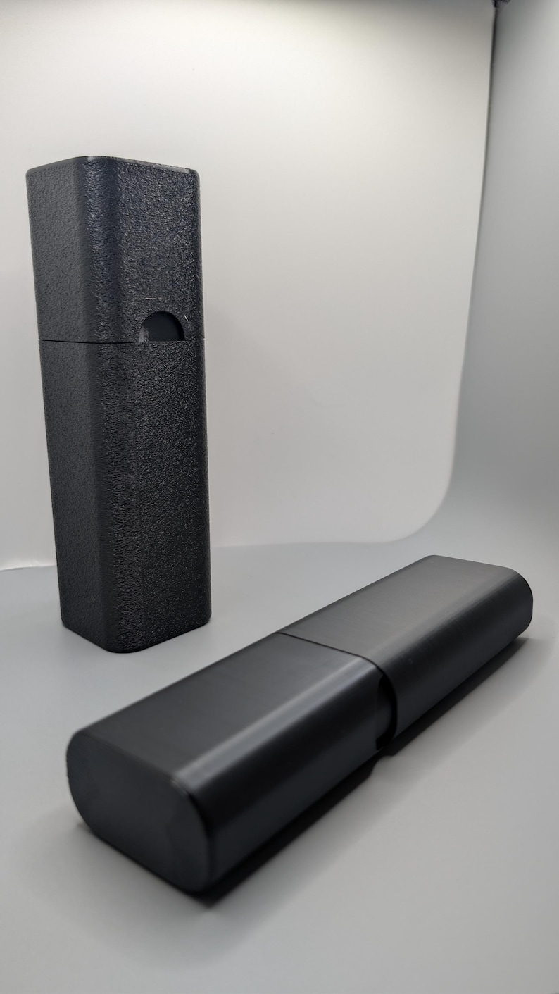 May include: Two black rectangular cases, one upright and the other lying horizontally. The upright case has a textured surface and a curved cutout. The horizontal case is smooth and appears to be hinged.