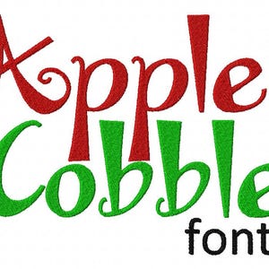 May include: The words "Apple Cobbler" in red and green script font, with the word "font" in black below. The text is embroidered on a white background. The letters are thick and rounded.