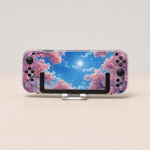 May include: A handheld gaming console featuring a decorative skin with a vibrant pink cherry blossom tree pattern against a bright blue sky with a sunburst. The device is held in a black plastic stand and includes standard black buttons.