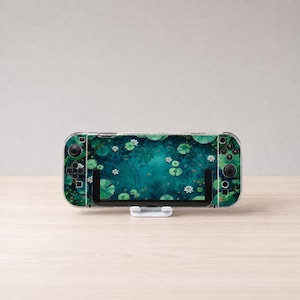 May include: A handheld gaming console featuring a decorative skin with a dark teal pond scene, including green lily pads and white water lily flowers. The device has black control buttons on the left and right sides and is held by a white stand.