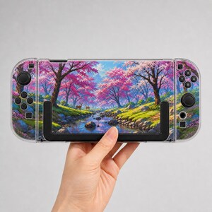 May include: A handheld gaming console featuring a vibrant landscape print of a stream flowing through a forest with bright pink cherry blossom trees and two deer. The device has black control sticks, directional buttons, and action buttons.