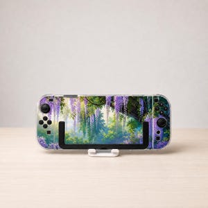 May include: A handheld gaming console featuring a decorative skin with a vibrant illustration of purple wisteria flowers hanging from tree branches over a lush green forest background, with black control buttons and joysticks on both sides.