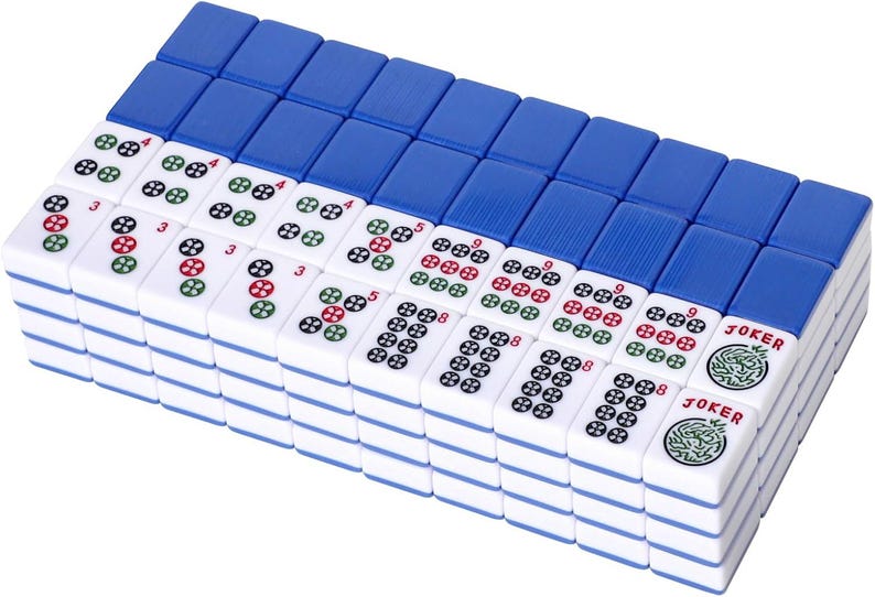 Puede incluir: Un conjunto de fichas de mahjong rectangulares dispuestas en cuadr&iacute;cula, con caras blancas y dorsos azules. Las fichas muestran varios patrones num&eacute;ricos en tinta roja, verde y negra, junto con dos fichas marcadas claramente con la palabra JOKER.