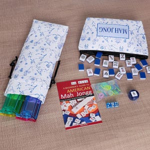 Puede incluir: Un juego de Mah Jongg que incluye una bolsa de tela blanca con motivos florales azules, un estuche con cremallera a juego con la etiqueta MAH JONGG, numerosas fichas blancas y azules, un libro de instrucciones rojo, fichas de pl&aacute;stico y dados.