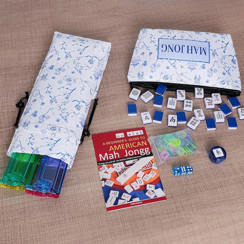 Puede incluir: Un juego de Mah Jongg que incluye una bolsa de tela blanca con motivos florales azules, un estuche con cremallera a juego con la etiqueta MAH JONGG, numerosas fichas blancas y azules, un libro de instrucciones rojo, fichas de pl&aacute;stico y dados.