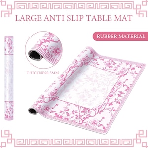 Puede incluir: Una alfombrilla de mesa antideslizante grande hecha de material de goma con un grosor de 3 mm. La alfombrilla presenta una superficie blanca con un patr&oacute;n floral rosa y un borde geom&eacute;trico. El texto LARGE ANTI SLIP TABLE MAT es visible arriba.