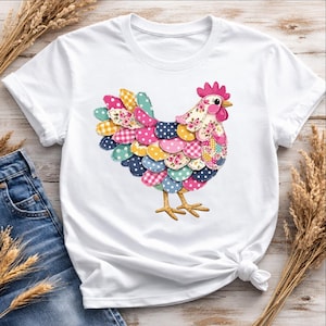 Op de afbeelding: Wit T-shirt met een kleurrijk patchwork kippenontwerp. De kip heeft een roze kam, een gele snavel en veelkleurige veren met bloemen-, stippen- en ruitpatronen. Het shirt wordt gecombineerd met een blauwe jeans en tarwearen.