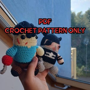 May include: Two crocheted dolls, one in a blue shirt and the other in a black and white outfit, are held in front of a window. The doll on the left has a red ball attached. The text "PDF CROCHET PATTERN ONLY" is displayed in red.