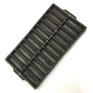 May include: A rectangular, cast iron cornbread pan with 24 individual molds. The pan is dark gray and has a slightly textured surface. It features two small handles on the sides and is designed for baking cornbread sticks.