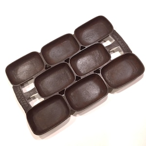 May include: A cast iron pan with eight rectangular molds. The pan is dark brown and has a textured surface. The handle is integrated into the design. This pan is ideal for baking small loaves of bread or cornbread.