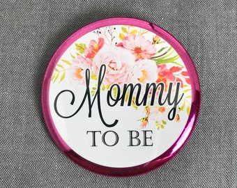 May include: Pink and white floral button with the text "Mommy to Be" in black.