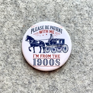 May include: White round button with a black and white image of a horse-drawn carriage. The text on the button reads "Please be patient with me I'm from the 1900s".